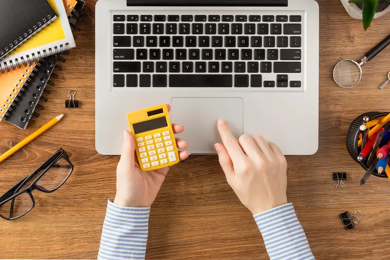 Plano cenital de una persona con una calculadora y un ordenador calculando cuánto cuesta el SEO al mes